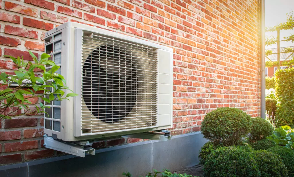 Side view of outdoor heat pump unit hanging on brick wall of house on a sunny day