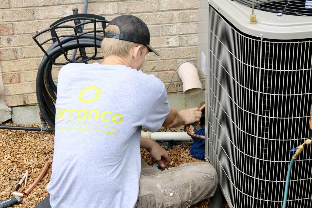 An Arronco Comfort Air technician working on an outdoor HVAC unit beside a home